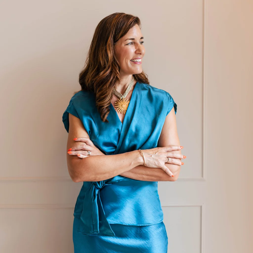 Selected Client Stories – Maaike van Ruitenbeek smiling in a blue dress, standing with her arms crossed.